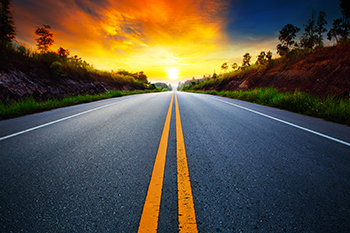 Asphalt road with greenery on sides facing the sunset representing Financial Planning